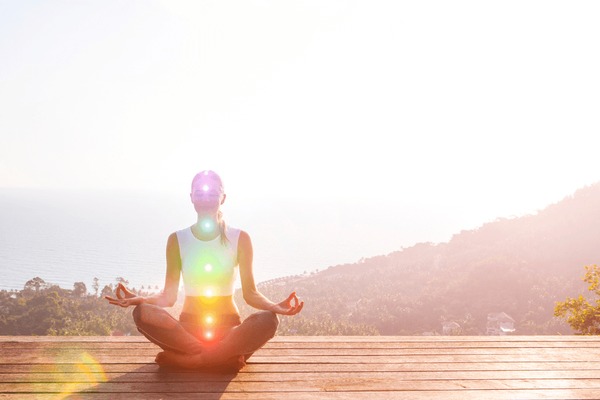 Beautiful woman sits in a pose of a half lotus on high place amazing view of the island outside, she practicing yoga meditation glowing seven all chakra eyes closed calm. Kundalini energy Stock Photo