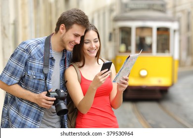 Couple of casual tourists consulting a paper guide and gps in a smartphone on line in the street of an old town Stock Photo