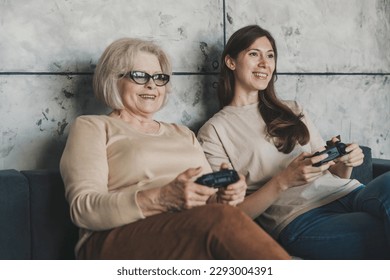 Video games competition in family between two women from different generations. Enjoying domestic hobby playtime with caring older mother. Stock Photo