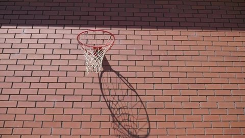 Front perspective of basket ball circling around metal ring and goes into hoop for goal on red brick wall background.