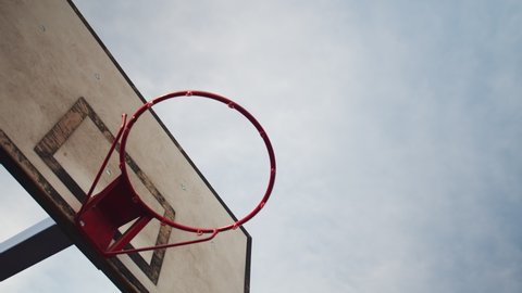 Basketball ball flying into a basketball hoop. View from under the basketball basket. Blue sky background. Basketball backboard on the outdoor sports field. Adlı Stok Video